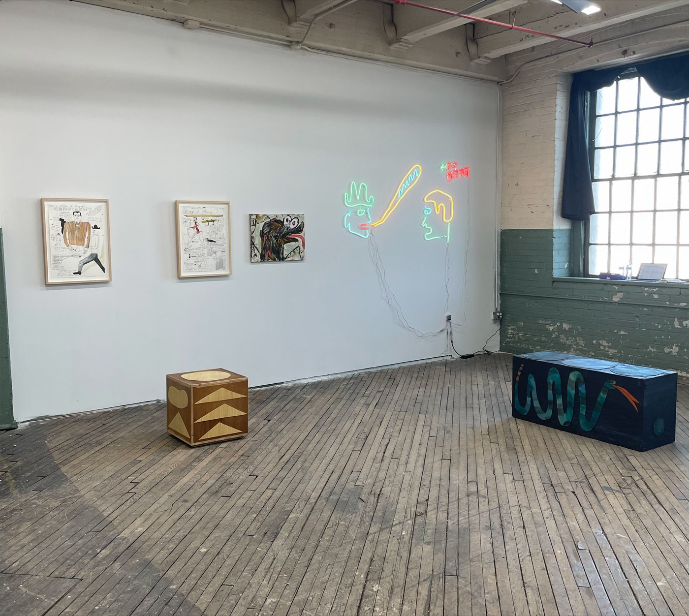 A studio at Rectangle Studios with drawings, a painting, a neon work, and painted sculpture on the wood floor.